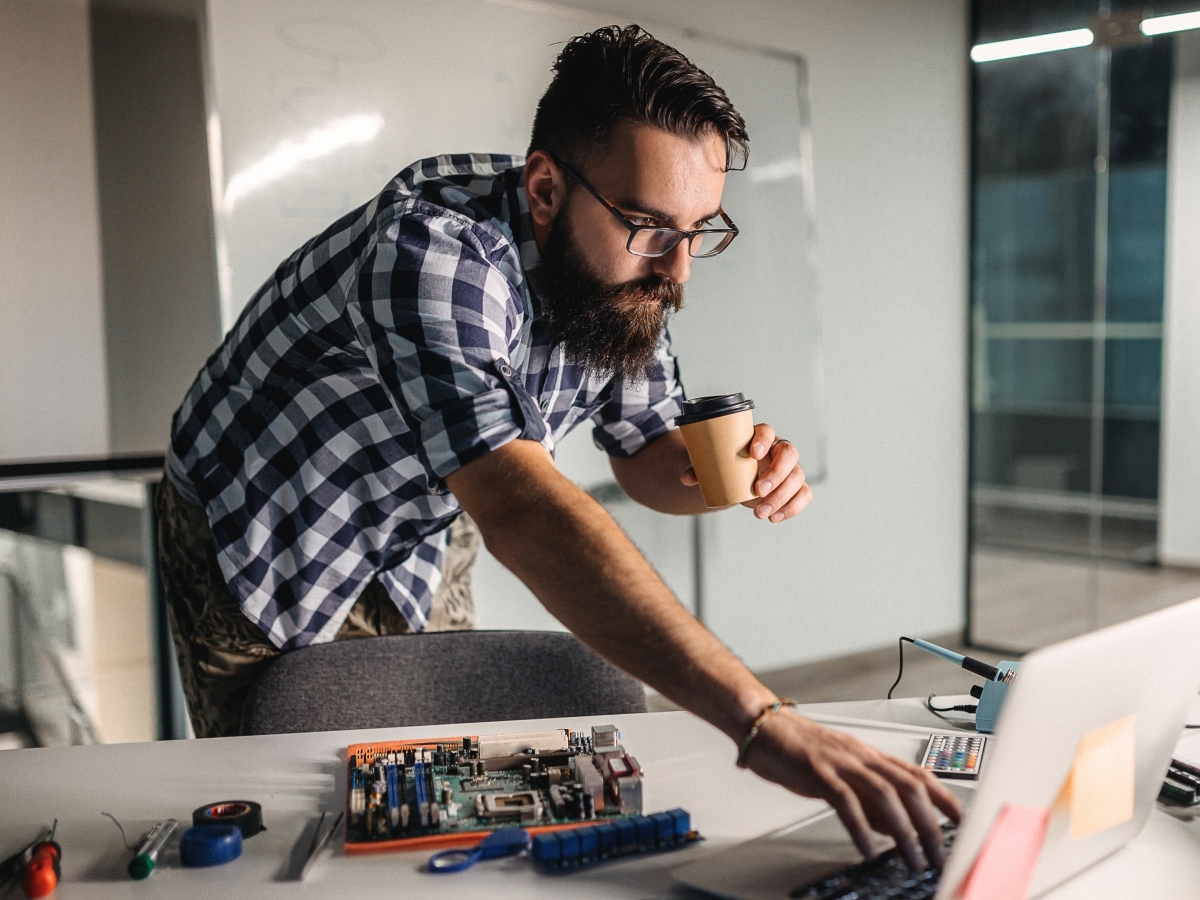 Heimwerker mit Kaffee am Arbeitstisch mit Platine und Laptop – Beratung für Bau & DIY mit homie AI
